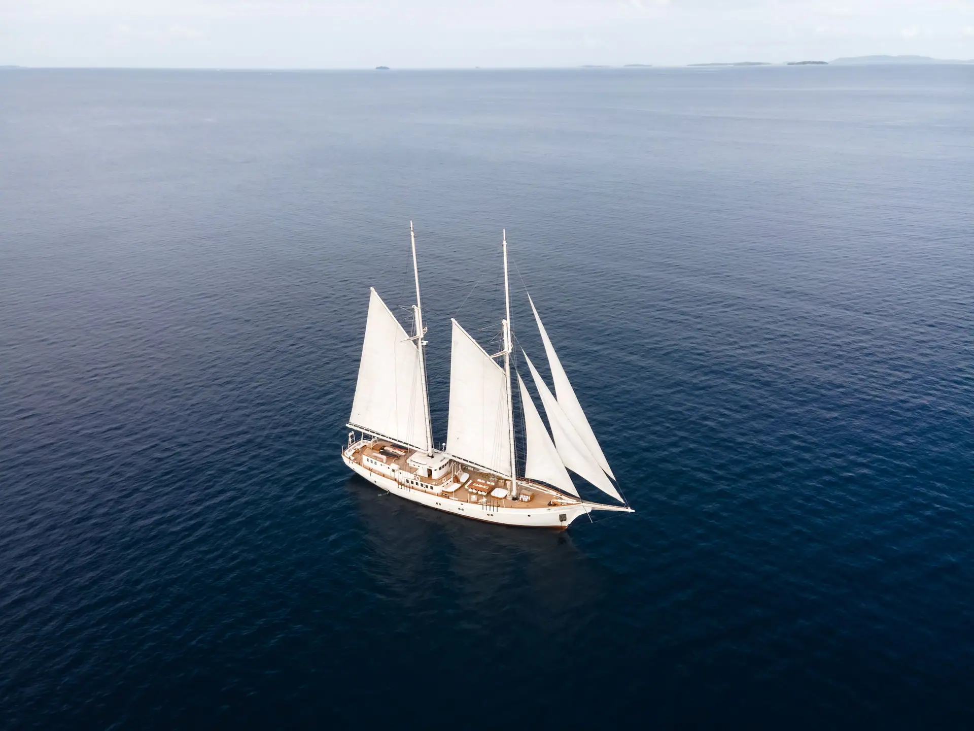 Aerial view of Mutiara Laut sailing on calm deep-blue water with all sails set