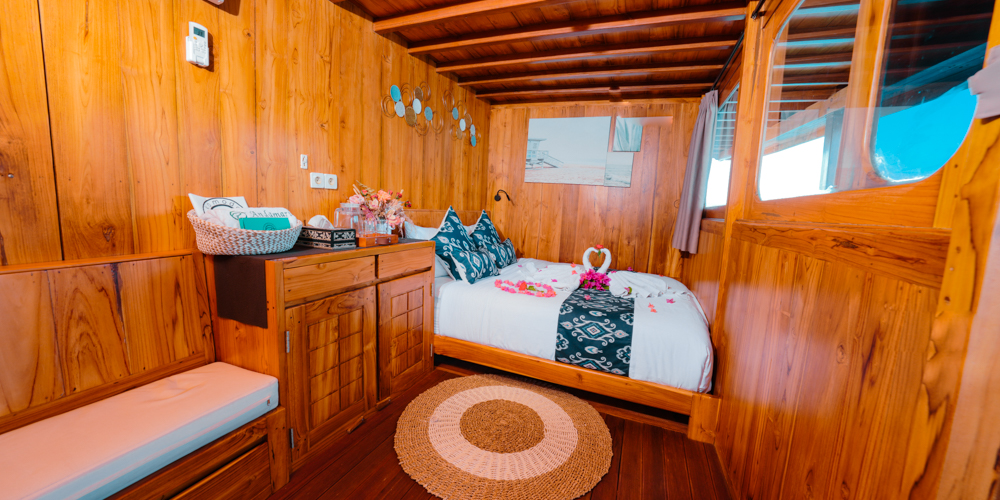 Warm teak double cabin on Andamari with bench seating, storage cabinet and floral bed styling