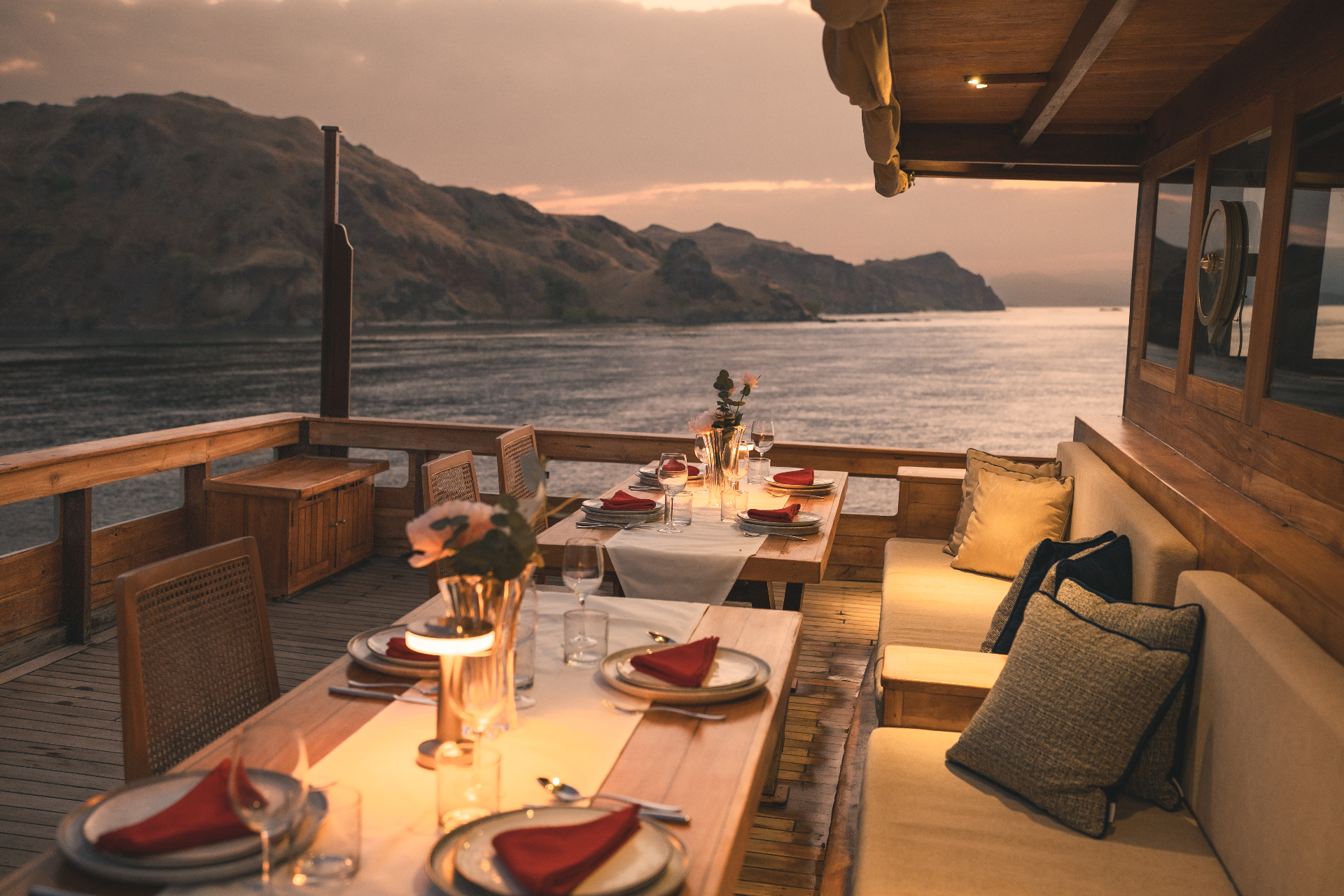 Candlelit outdoor dining on Mischief at dusk with Komodo hills and calm water in the background