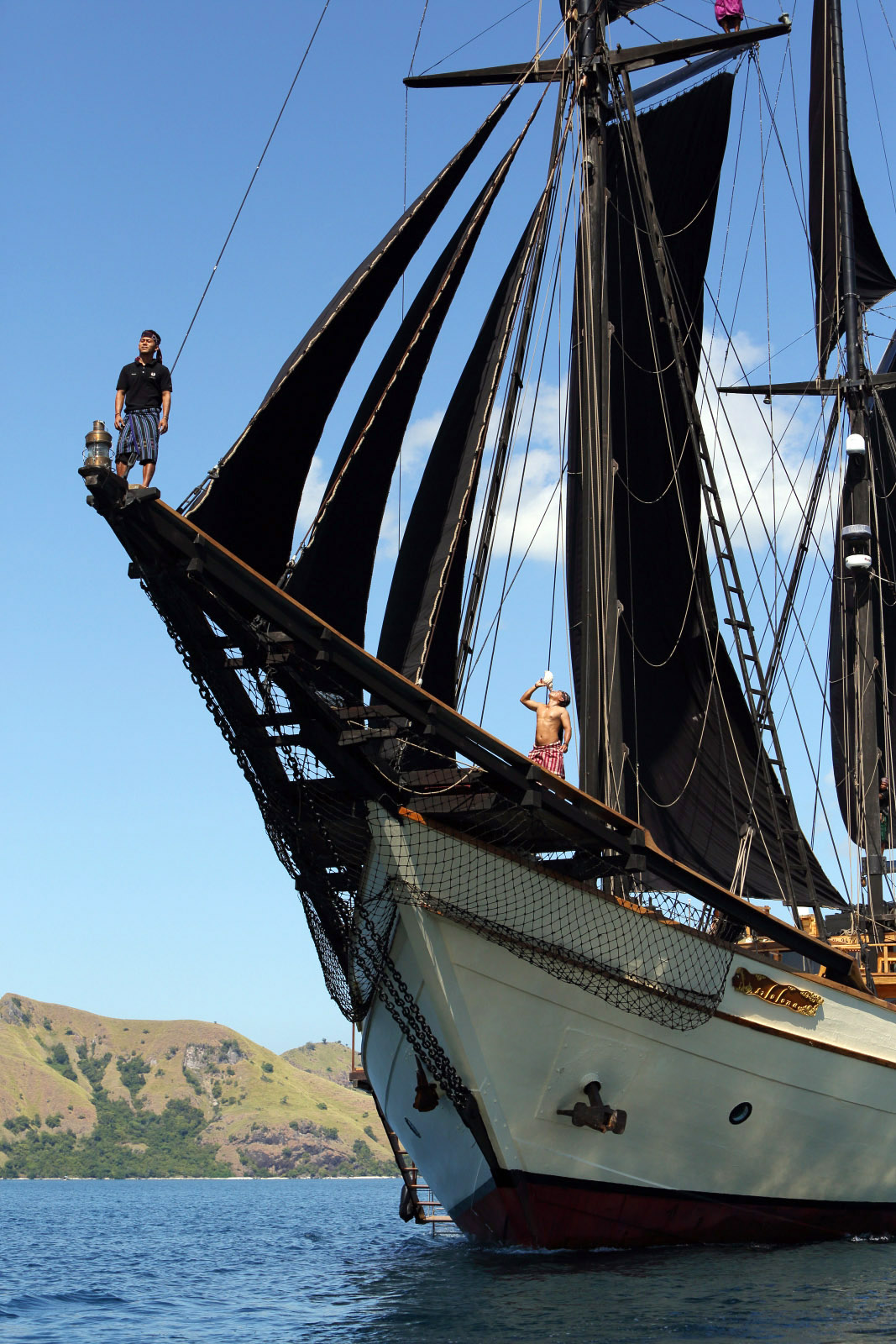 Crew member perched on Silolona's bowsprit as the yacht approaches a Komodo island