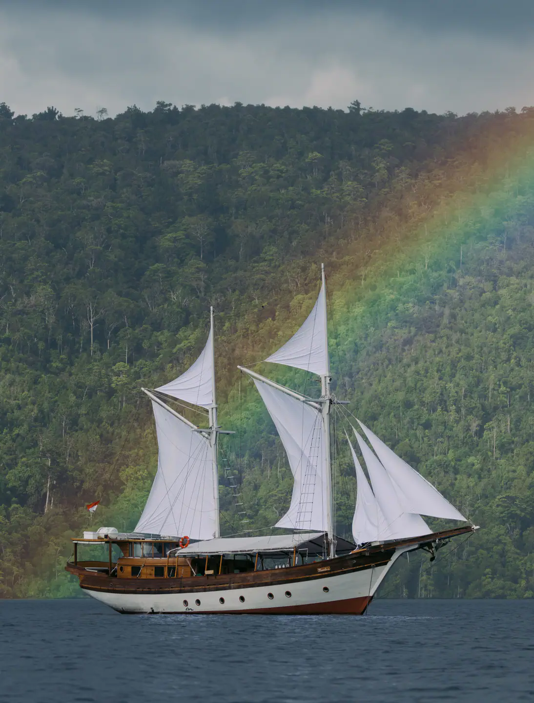 Anne Bonny sailing along a jungle-covered Raja Ampat coast