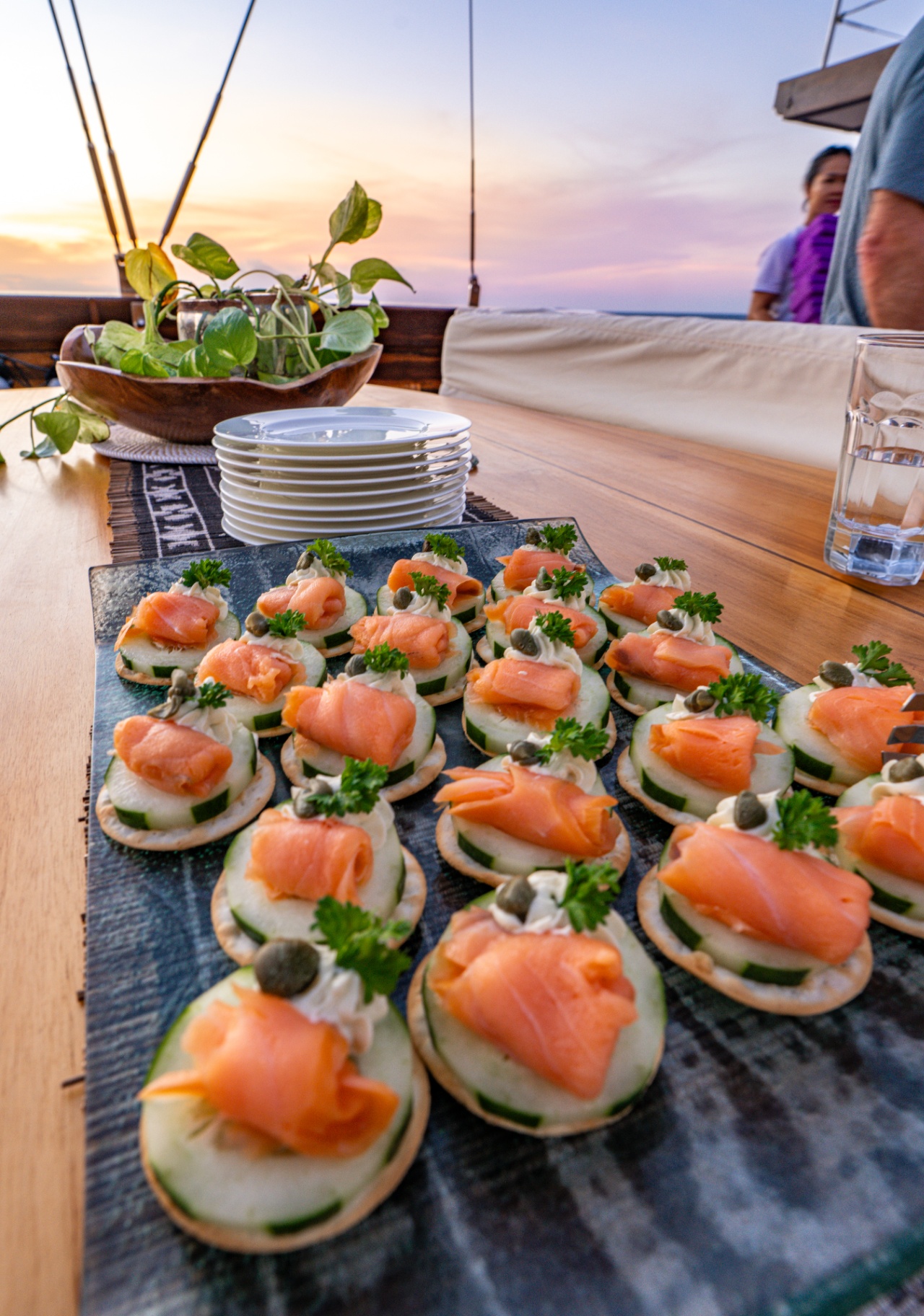 Smoked salmon and cucumber canapés with capers arranged on slate at sunset on Lamima's deck