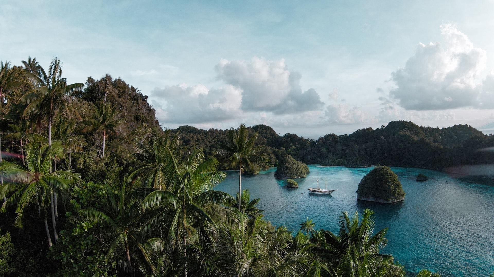 Senja anchored in a hidden Raja Ampat lagoon framed by palms and jungle karst islands