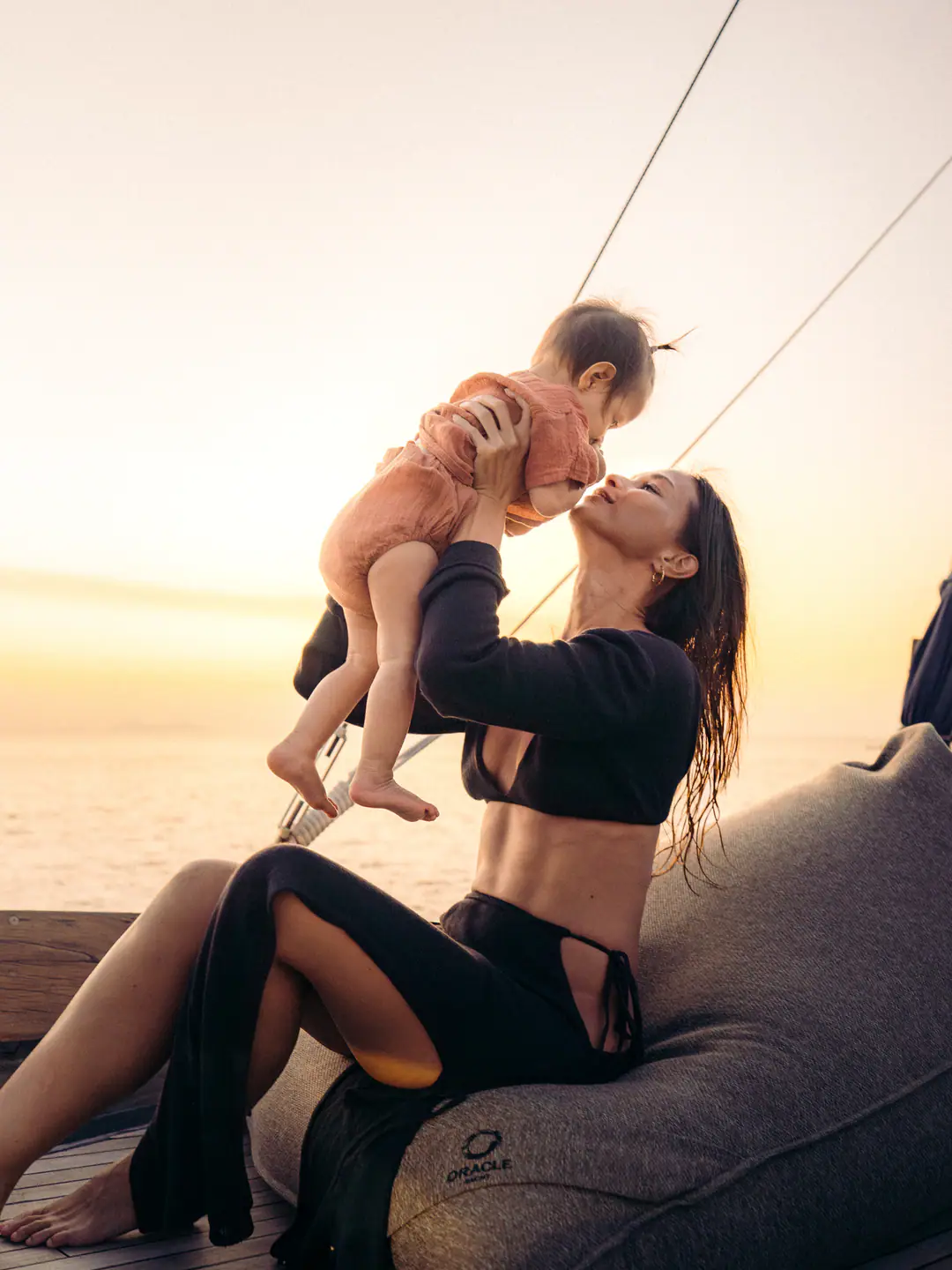 Mother lifting her baby against a golden sunset on The Oracle's deck