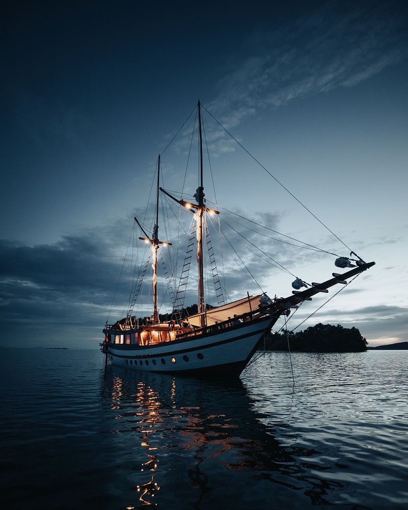 Bow-on view of Senja lit up at blue hour with warm cabin lights reflecting on still water