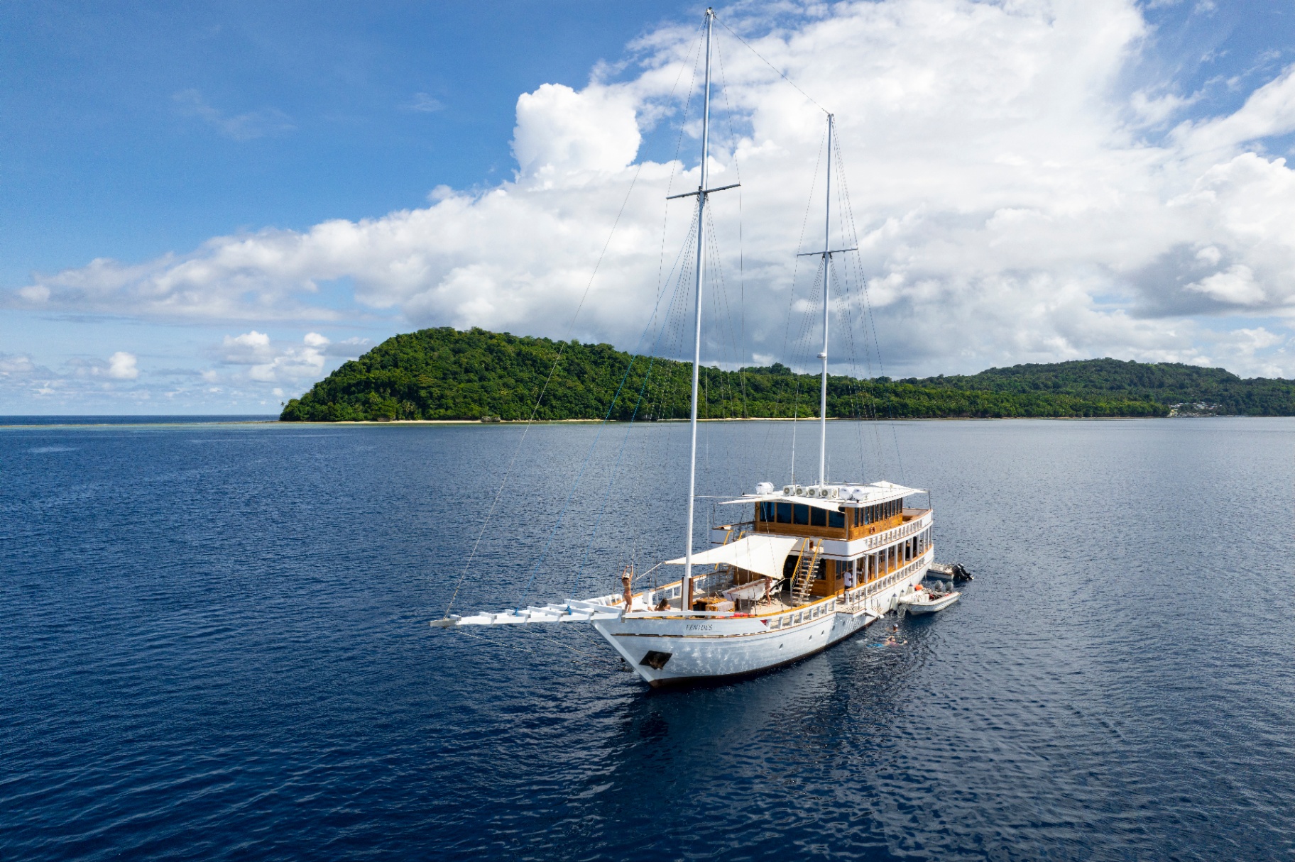 Fenides Liveaboard phinisi at anchor in a Raja Ampat bay with jungle-covered island behind