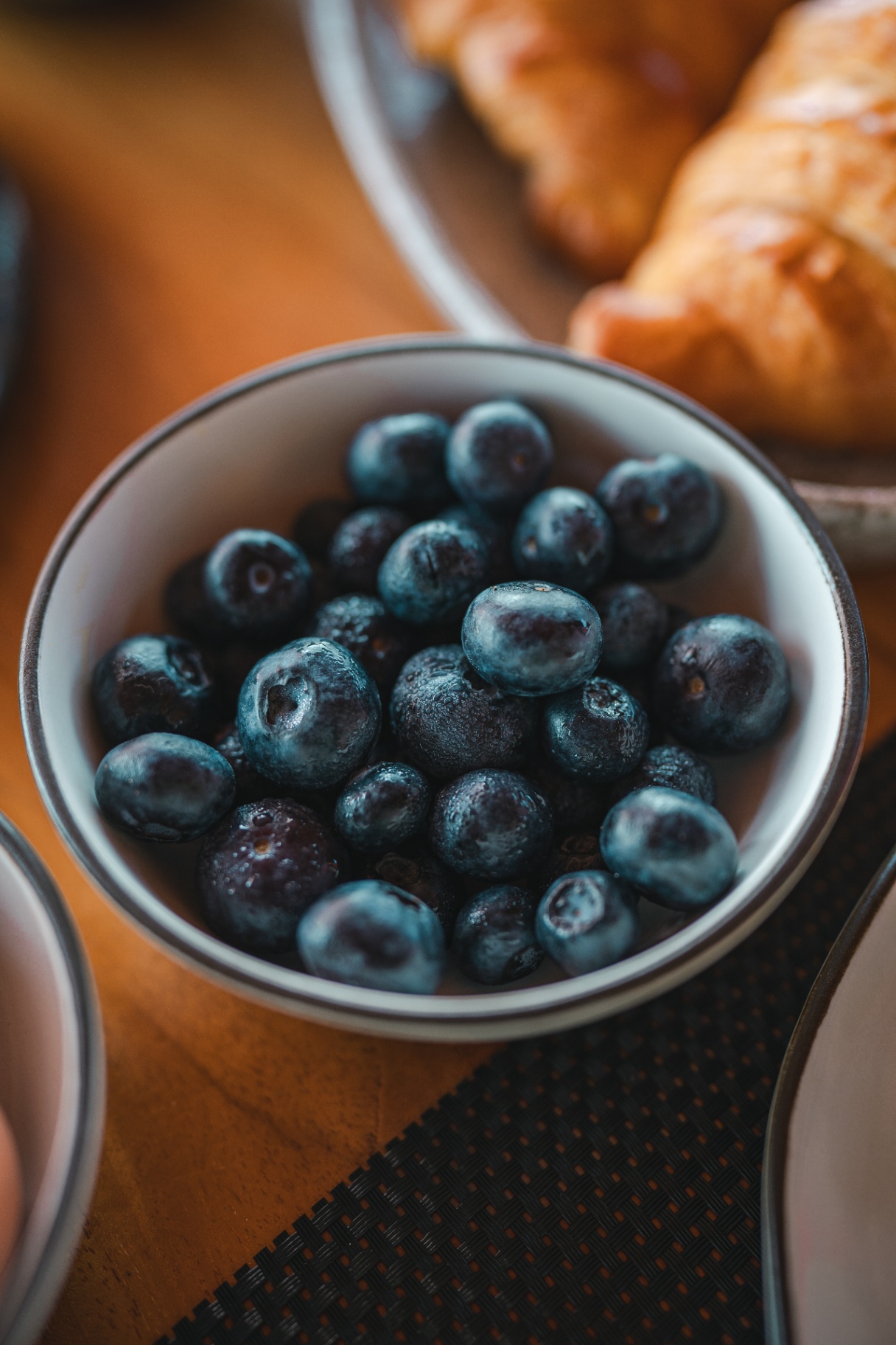 Bowl of fresh blueberries on Mischief's breakfast table beside a plate of golden croissants