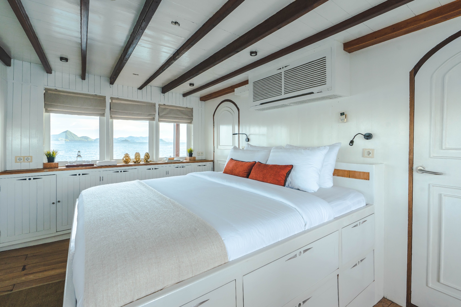 Banda cabin king bed with orange cushions, storage cabinetry and picture windows framing Komodo islands