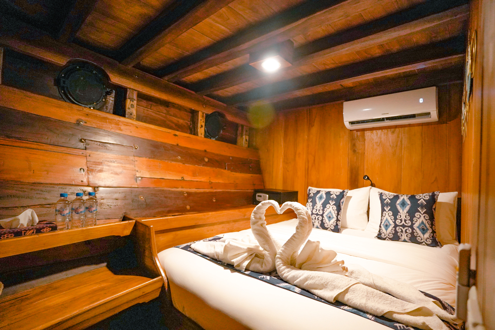 Double guest cabin on Adishree with teak-panelled walls, ikat cushions and swan-folded towels on a white bed