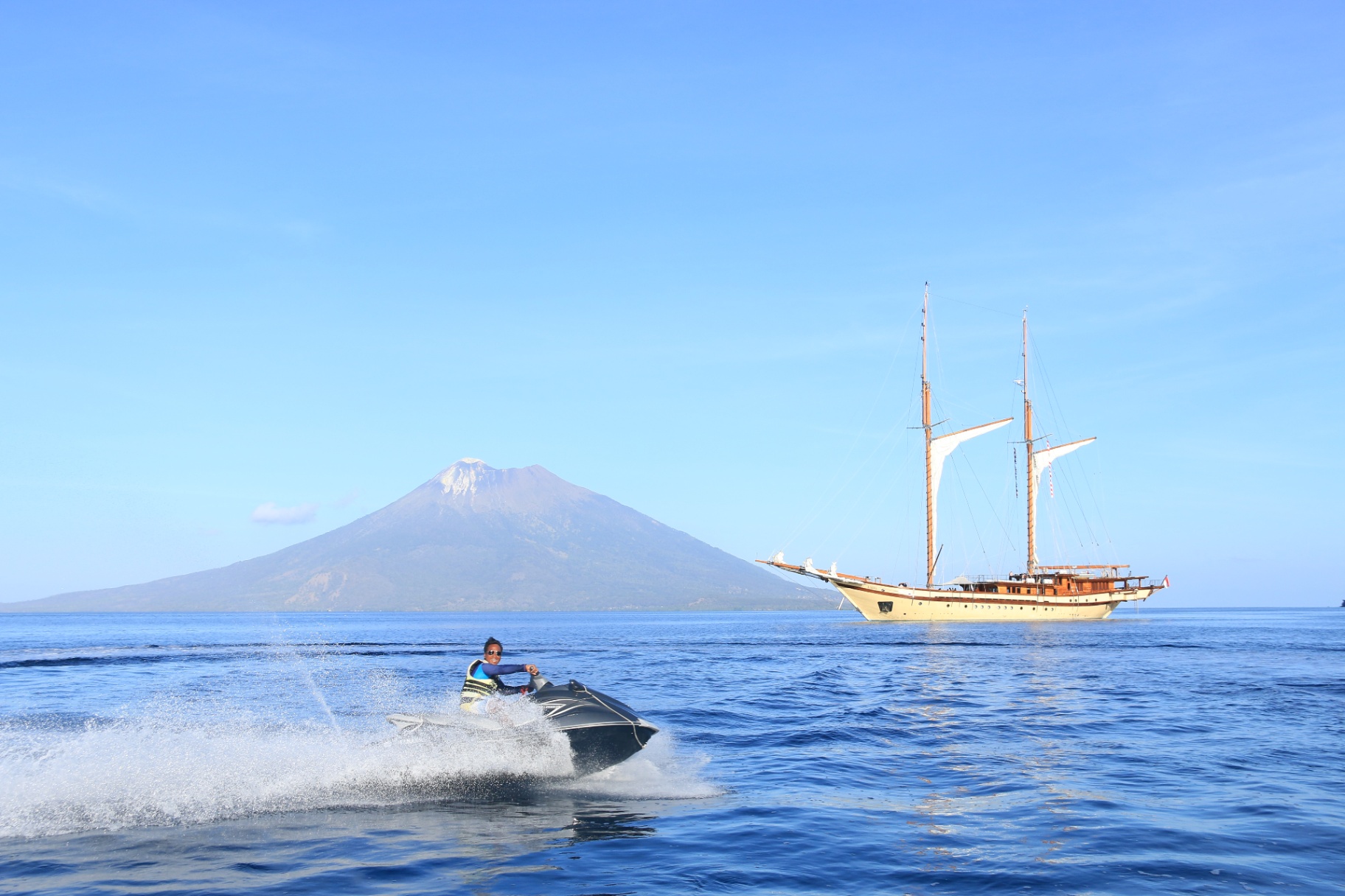 Guest riding a jetski across calm water with Lamima and a distant volcano behind