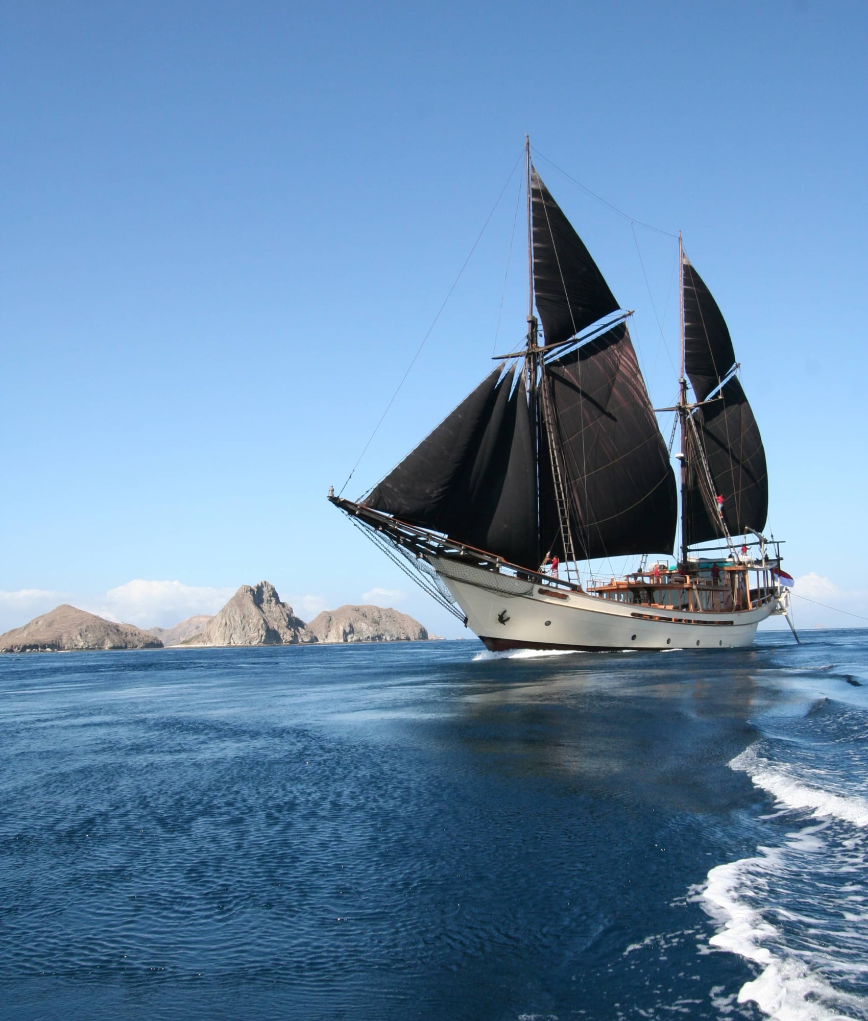 Silolona luxury phinisi sailing under black gaff-rigged sails past limestone islets in Komodo