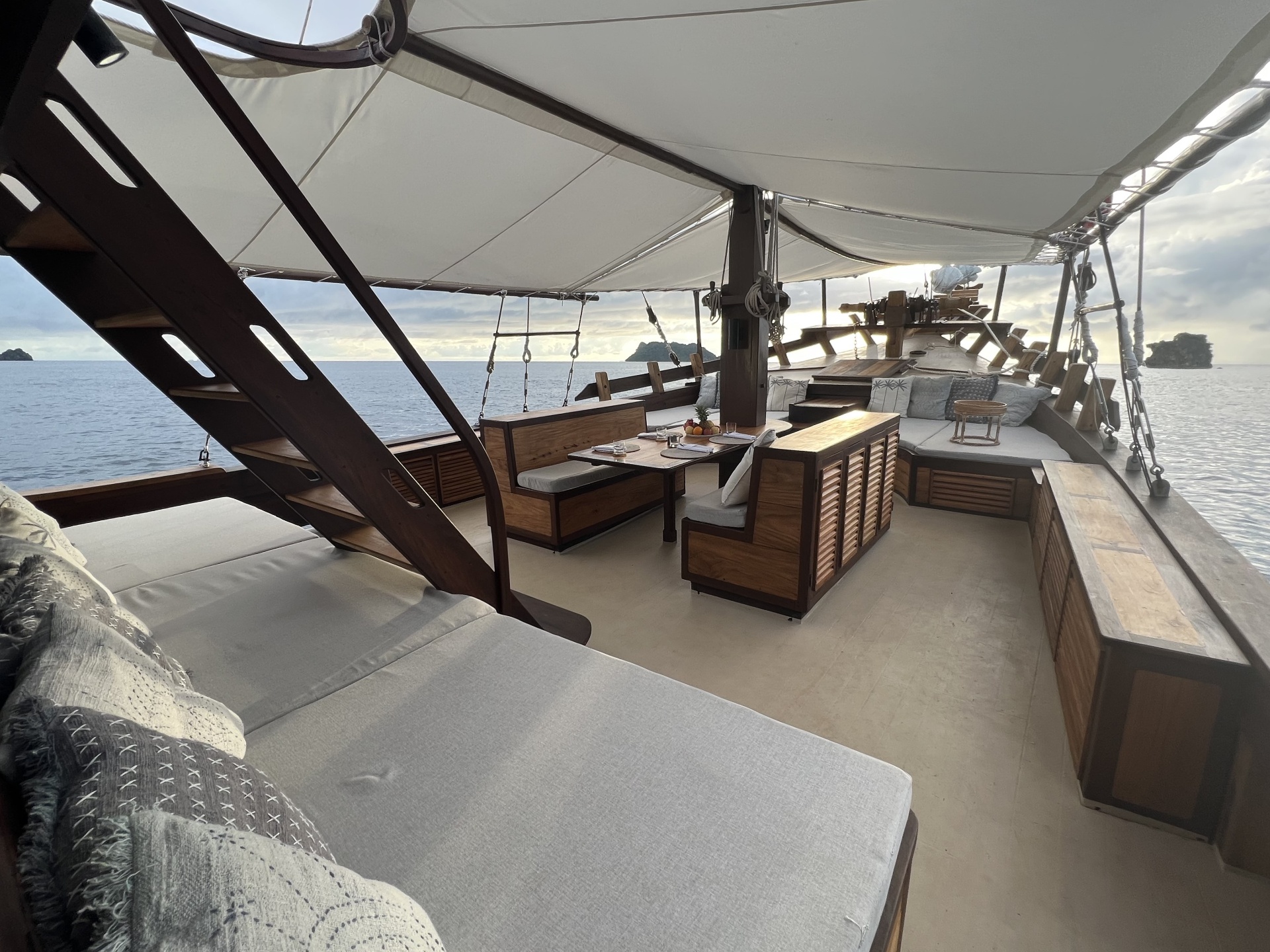 Wide view of Dewata's foredeck lounge and dining table with sunset sea beyond