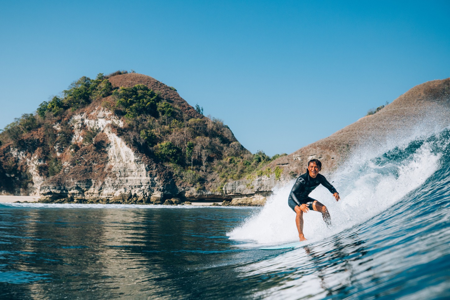 Surfer riding a clean wave with a limestone headland behind