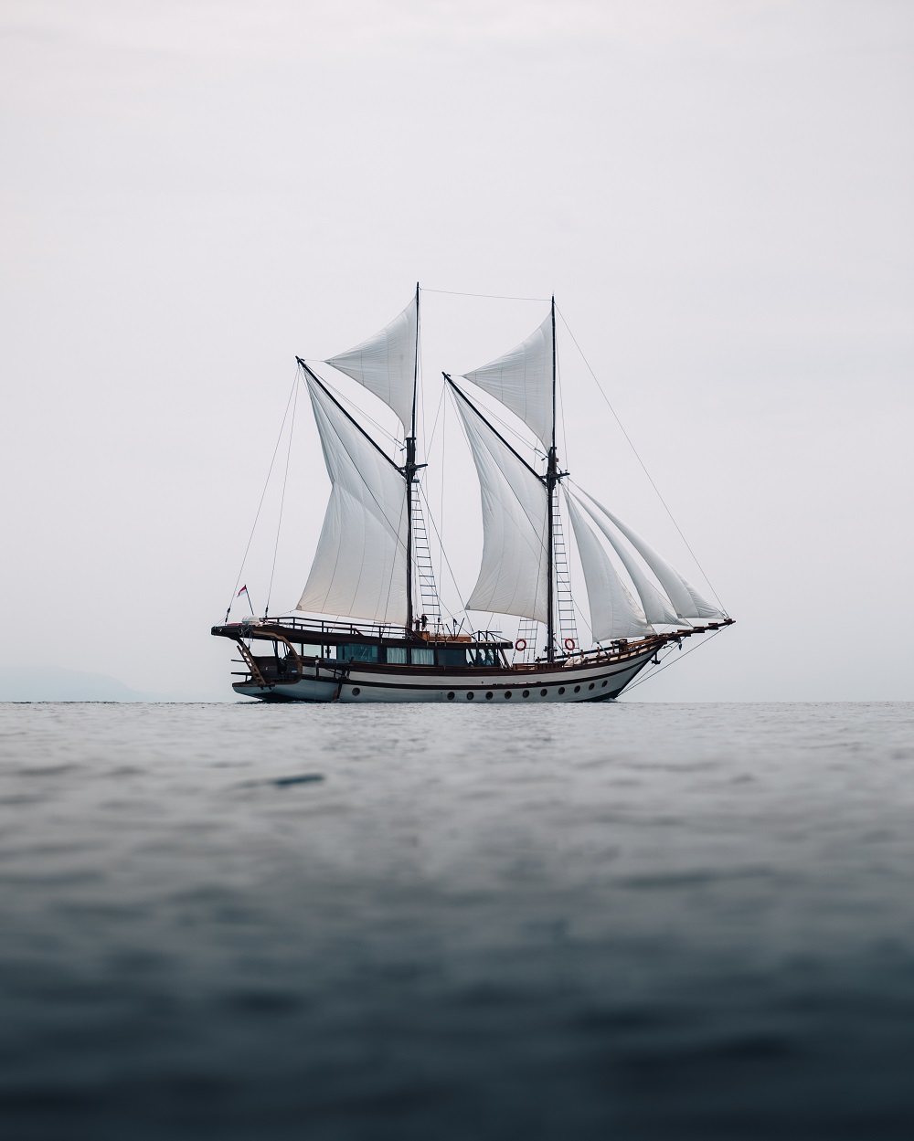 Senja under sail on calm water beneath a soft grey sky