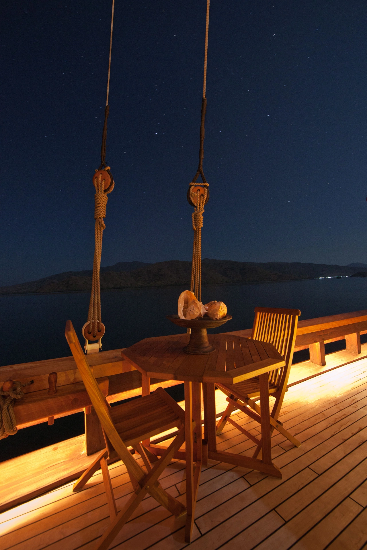 Warmly lit teak deck on Si Datu Bua at night under a starlit sky