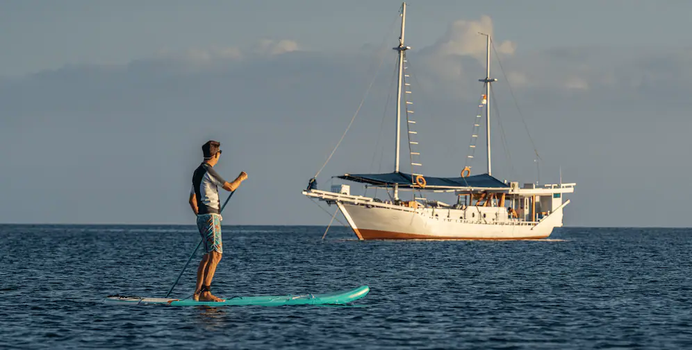 Guest paddleboarding at sunrise with Jinggo Janggo anchored behind