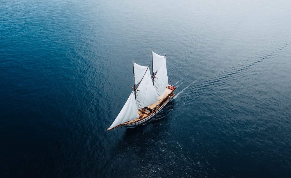 Aerial of Senja under white sails leaning slightly on open blue water