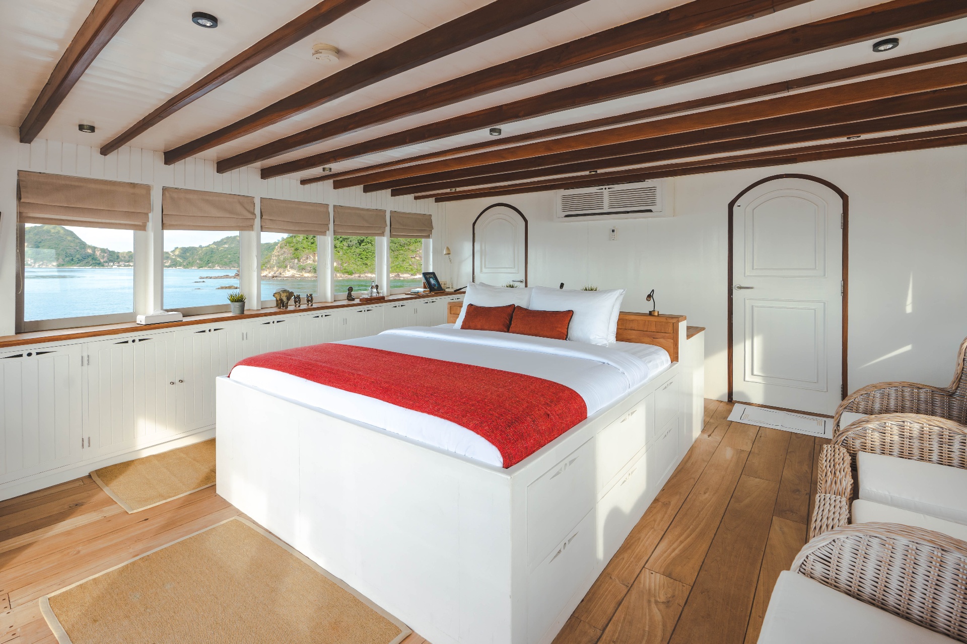 Bright Komodo suite interior on Mischief with king bed, wicker armchairs, storage cabinetry and Komodo island views