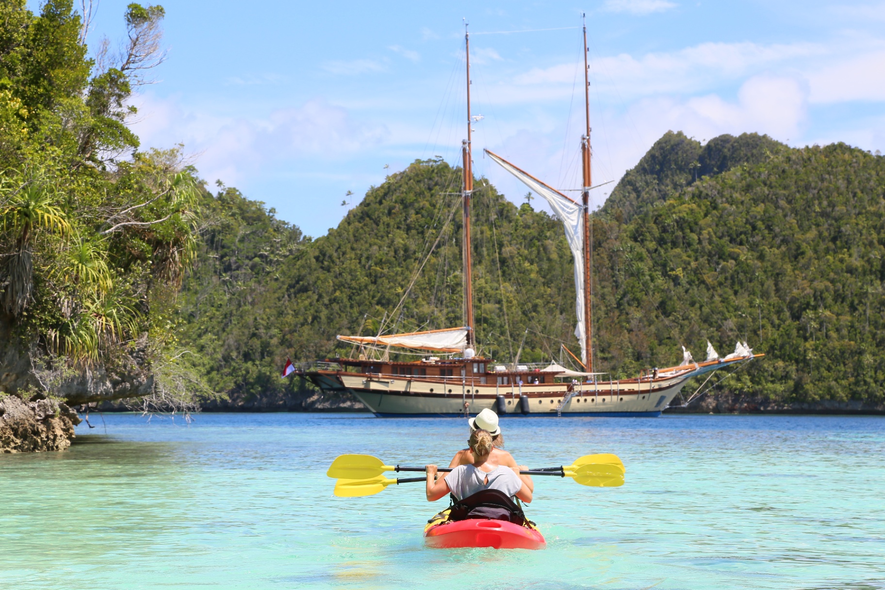 Two guests kayaking through a Raja Ampat karst lagoon toward Lamima anchored in the bay