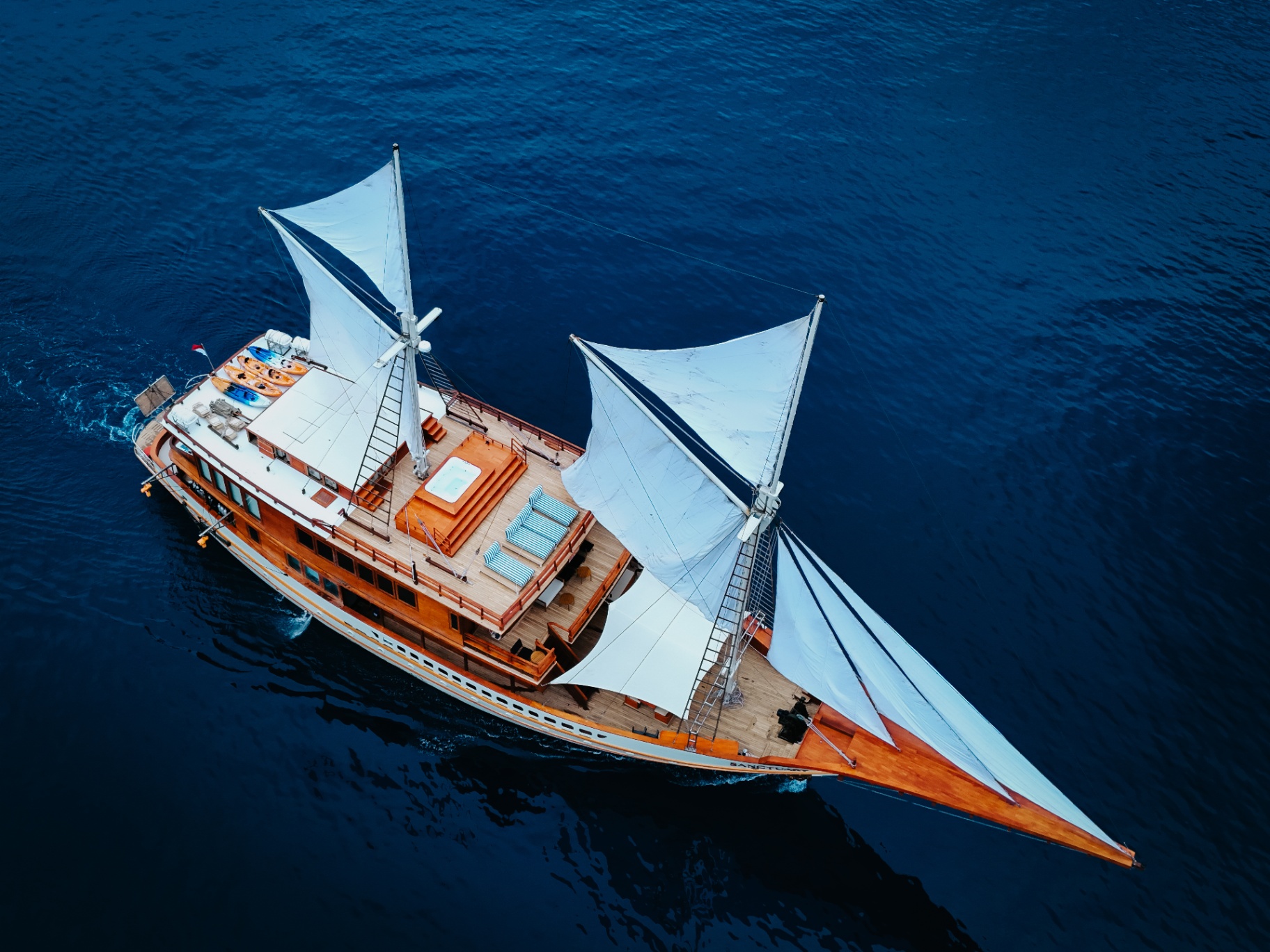 Aerial of Sanctuary phinisi under full white sails on deep blue Raja Ampat water