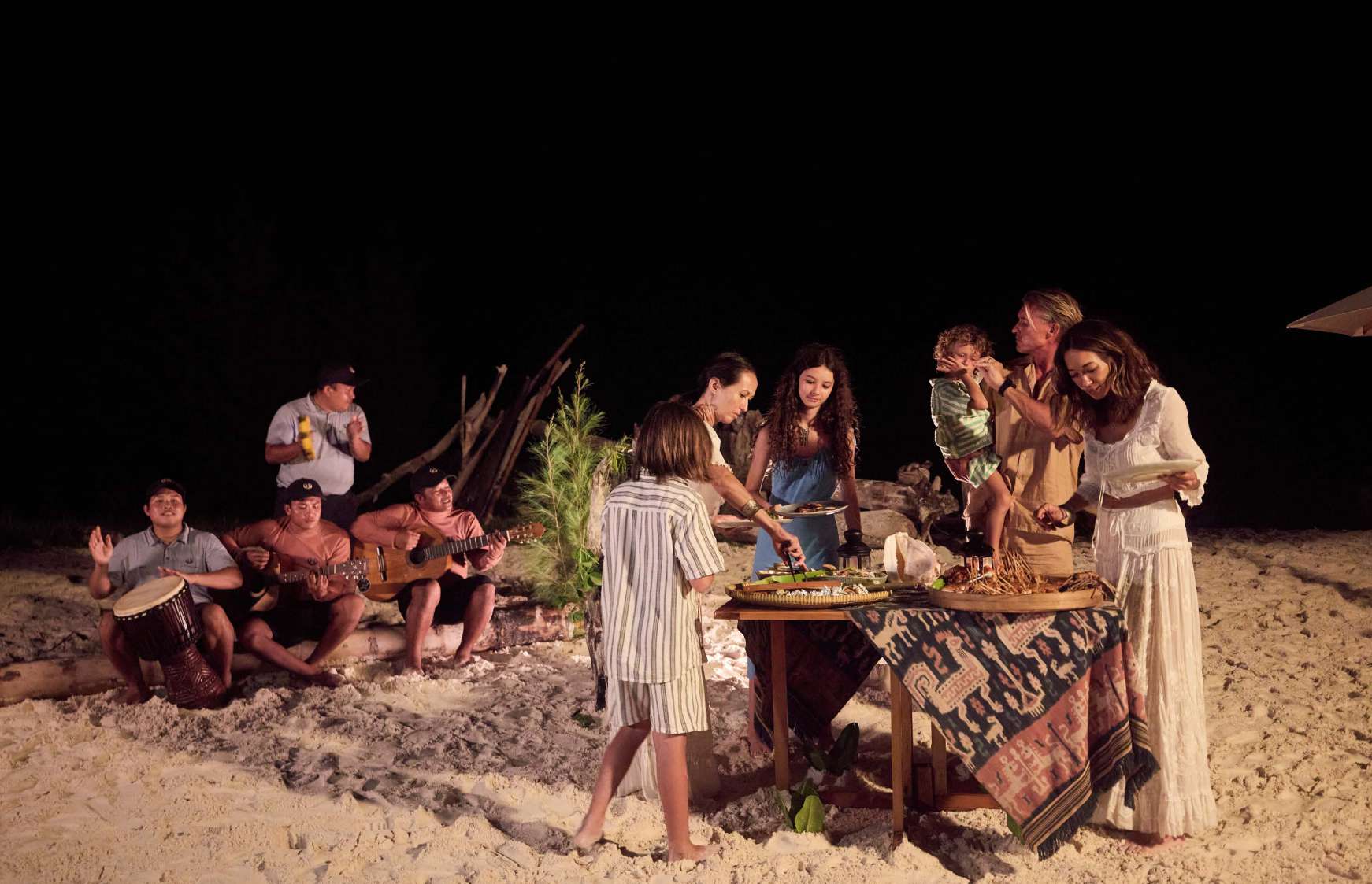 Family enjoying a lantern-lit beach dinner with musicians during a Si Datu Bua charter