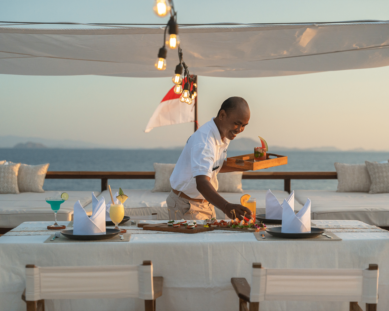 Crew member serving sunset drinks and canapes on Sanya's upper deck dining table