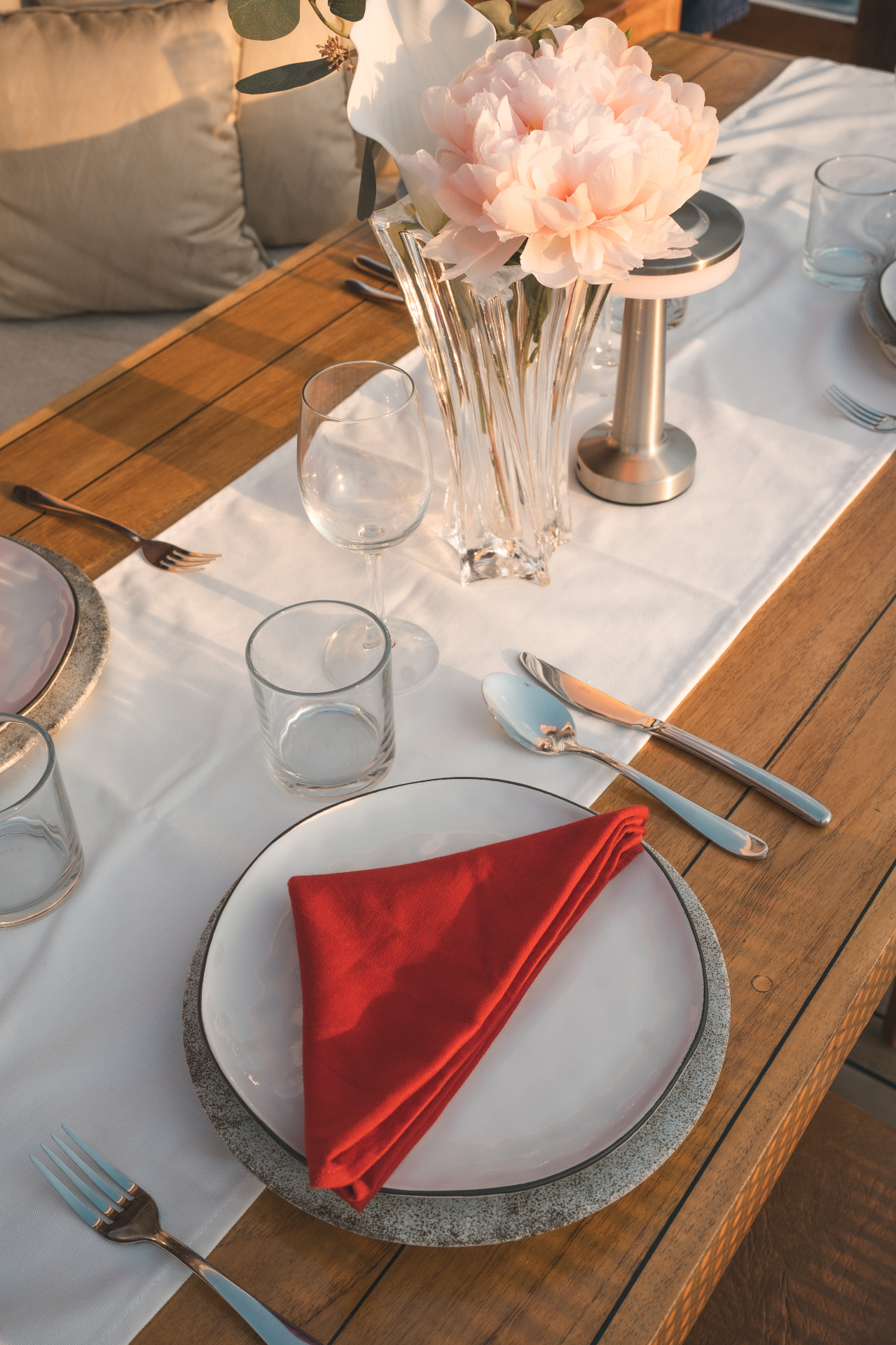 Close-up of Mischief's alfresco dining table dressed with flowers, crystal glassware and red linen napkins
