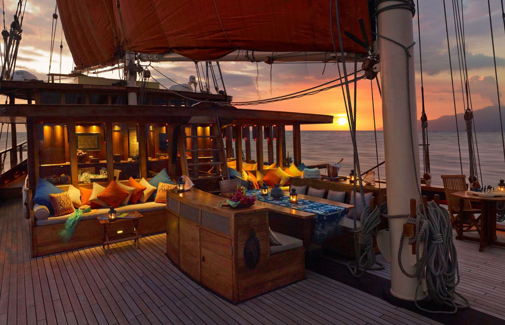 Aft-deck lounge on Si Datu Bua at sunset with colourful cushions, dining table and chess set