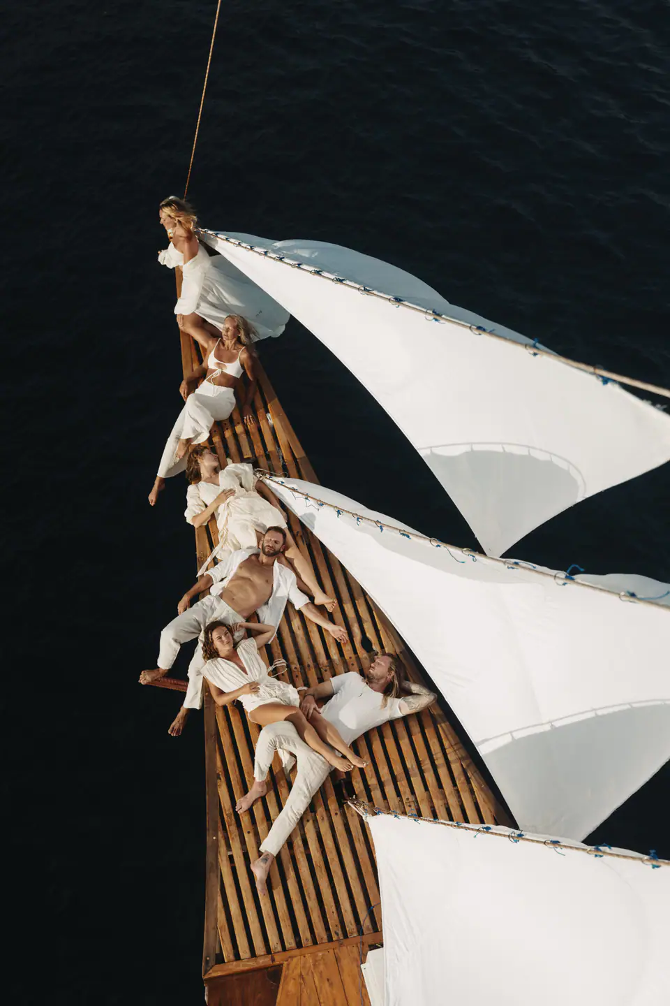 Friends dressed in white relaxing on Anne Bonny's bowsprit at sunset