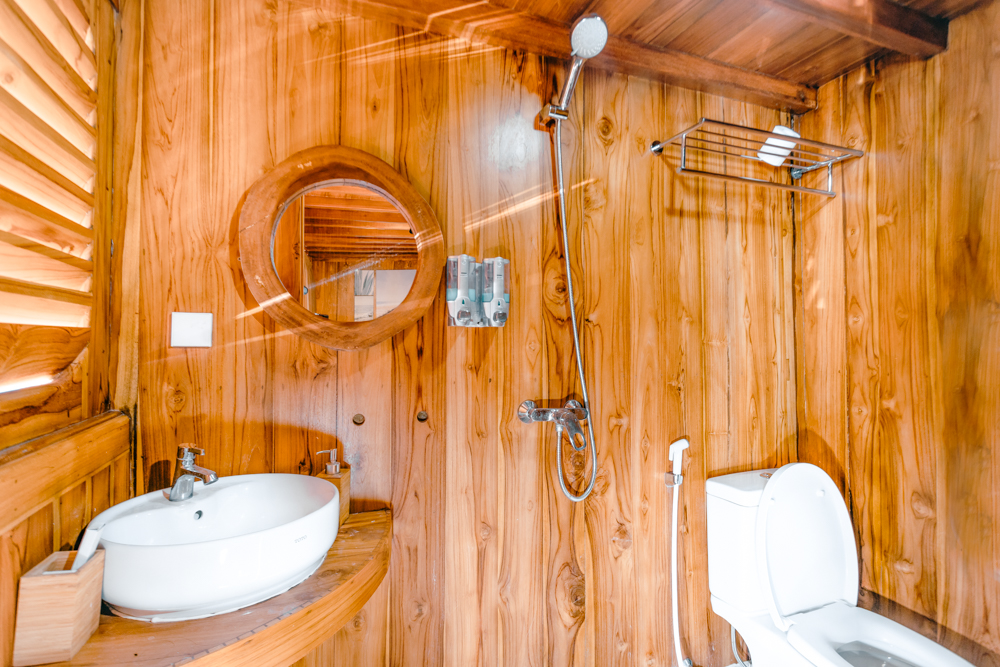 Ensuite bathroom on Andamari with round mirror, vessel sink, shower and teak walls
