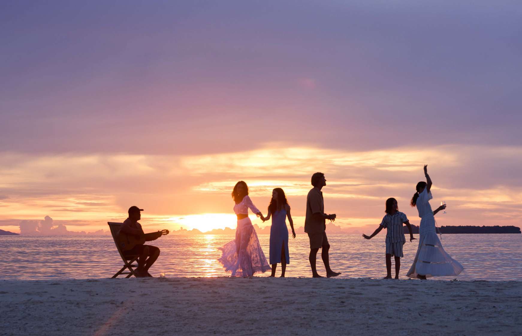 Guests dancing and playing guitar on a beach at sunset during a Si Datu Bua charter
