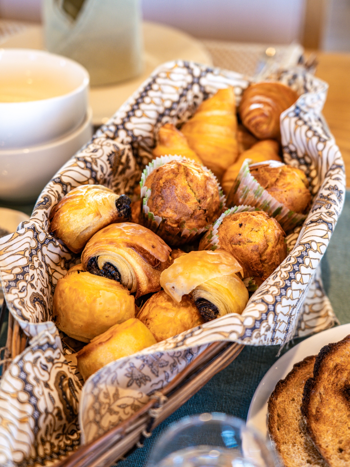 Basket of fresh croissants, pain au chocolat and muffins on a batik cloth at breakfast on Lamima