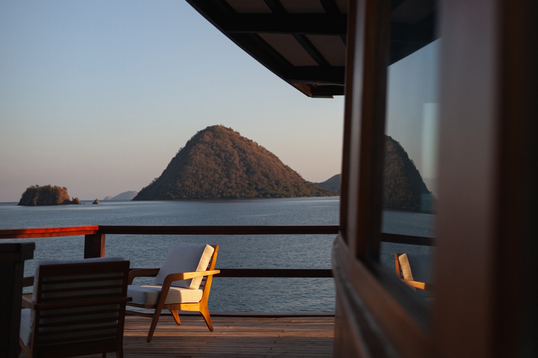Bridge deck lounge chairs on teak with a golden-hour view of a Komodo island