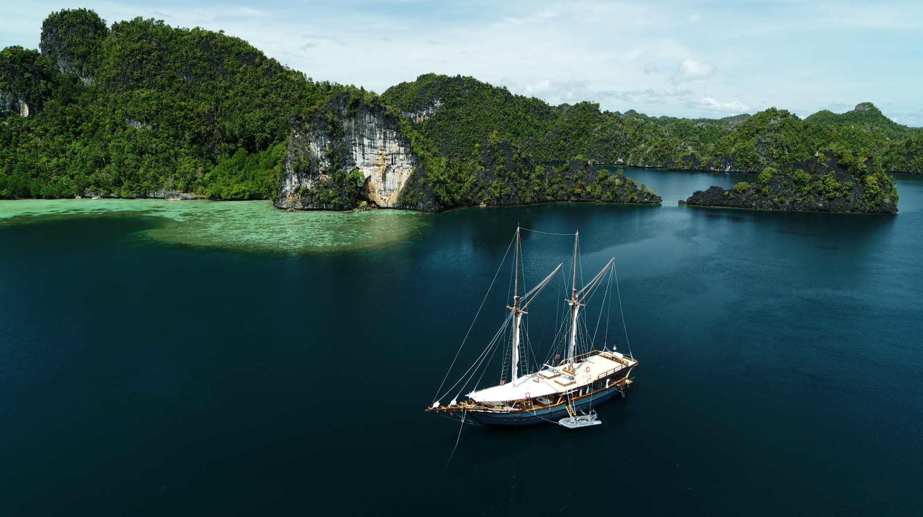 Aerial view of Dewata phinisi anchored beside a Raja Ampat karst cliff