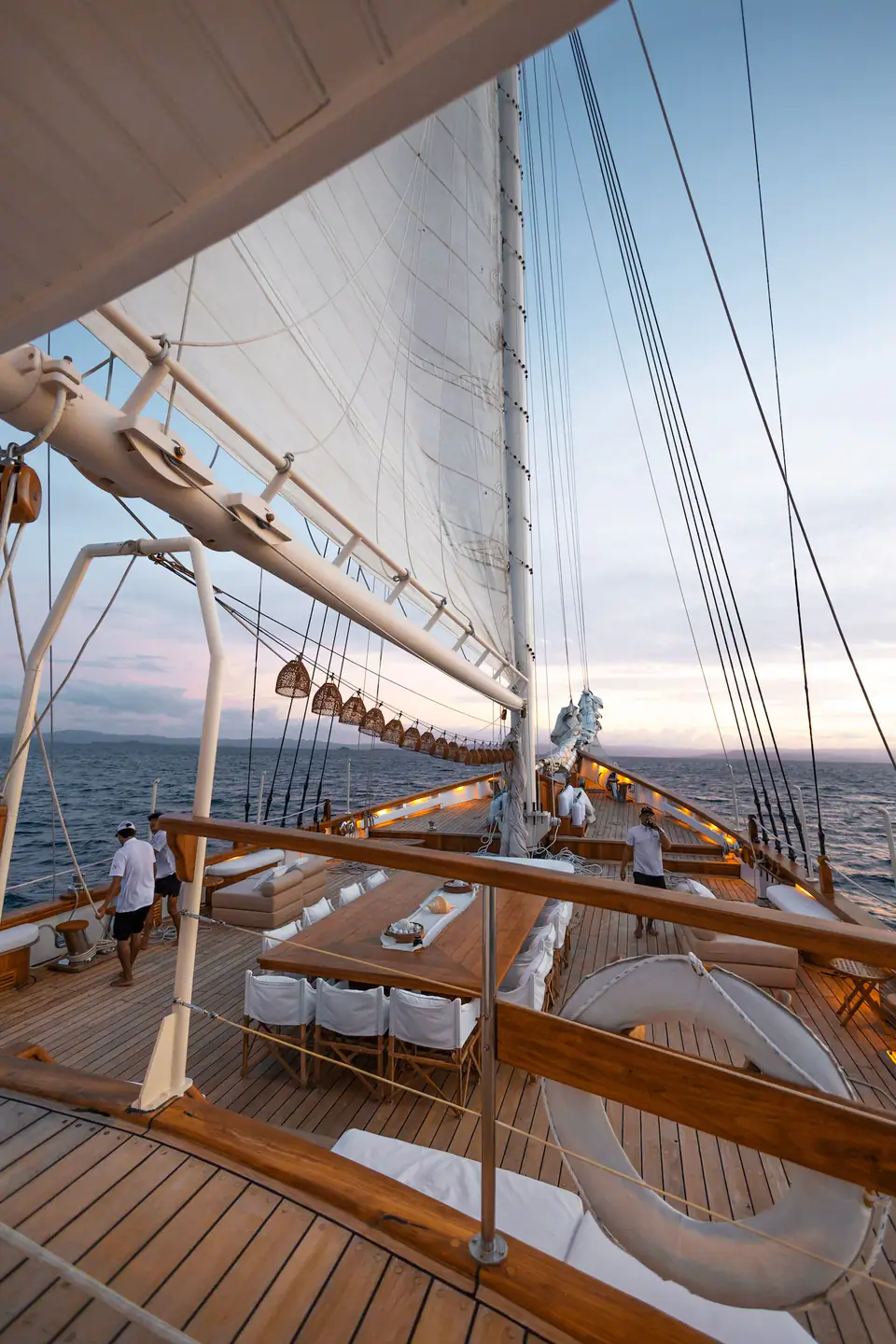 Crew working the deck of Mutiara Laut at dusk with lanterns lit