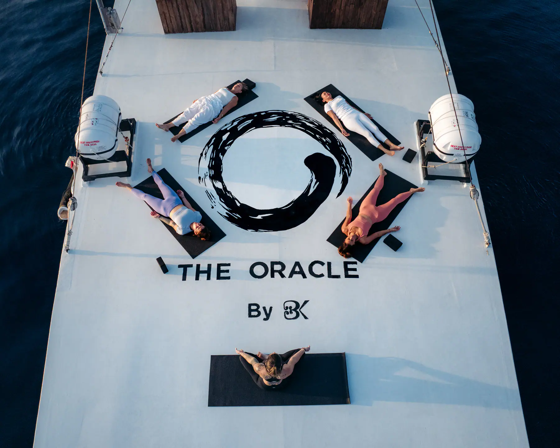 Aerial view of sunrise yoga class on The Oracle's foredeck around the enso circle logo