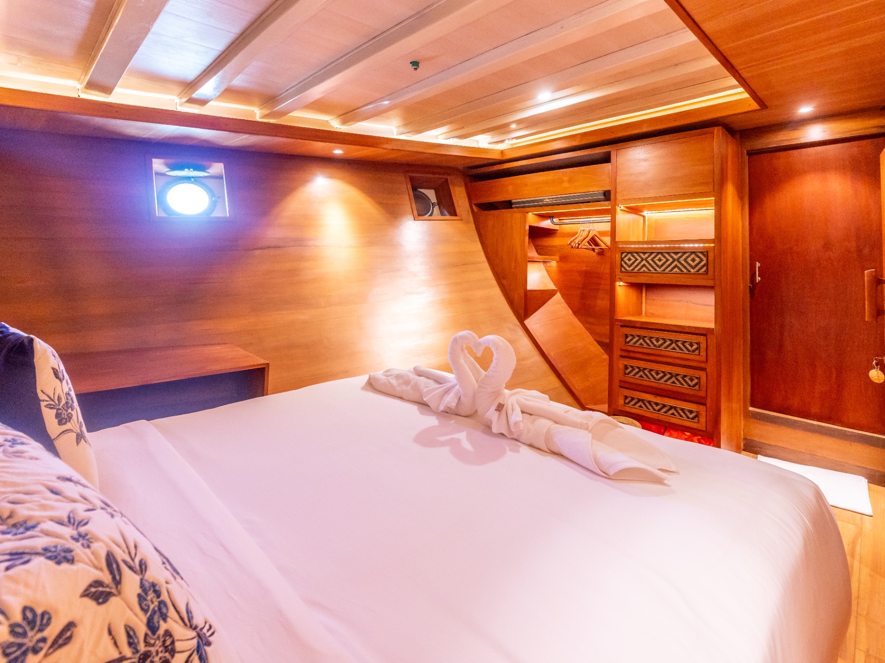 Lower-deck cabin on Sanctuary with double bed, porthole window and open walk-through wardrobe
