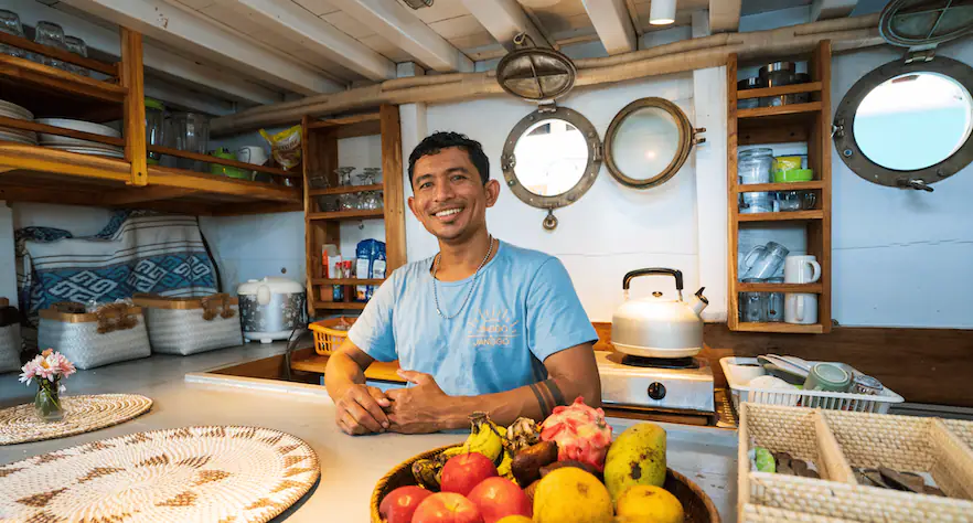 Jinggo Janggo cook smiling in the galley with fresh fruit on the counter