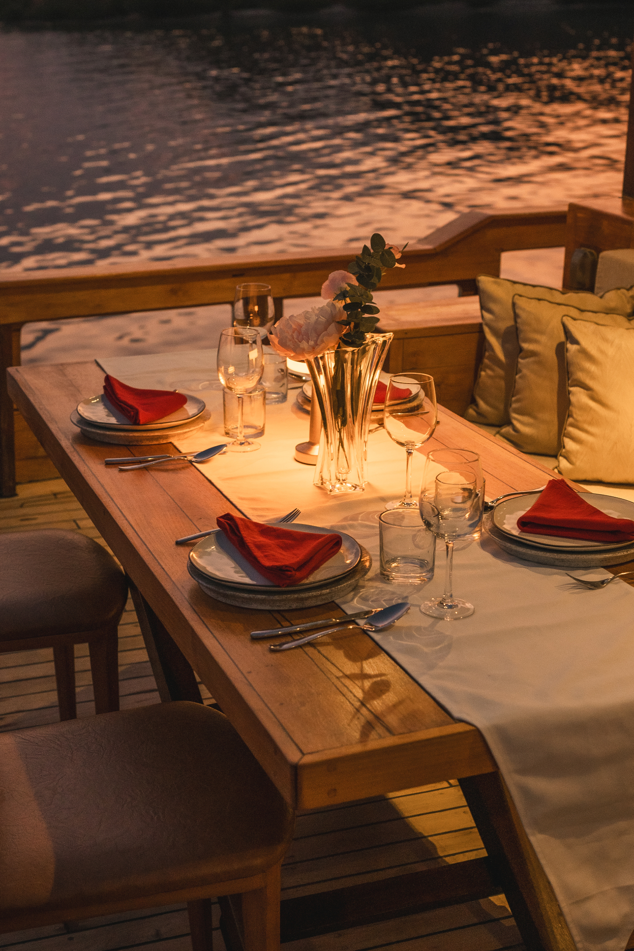 Close-up of Mischief's glowing dinner table with floral centrepiece, wine glasses and red napkins after sunset