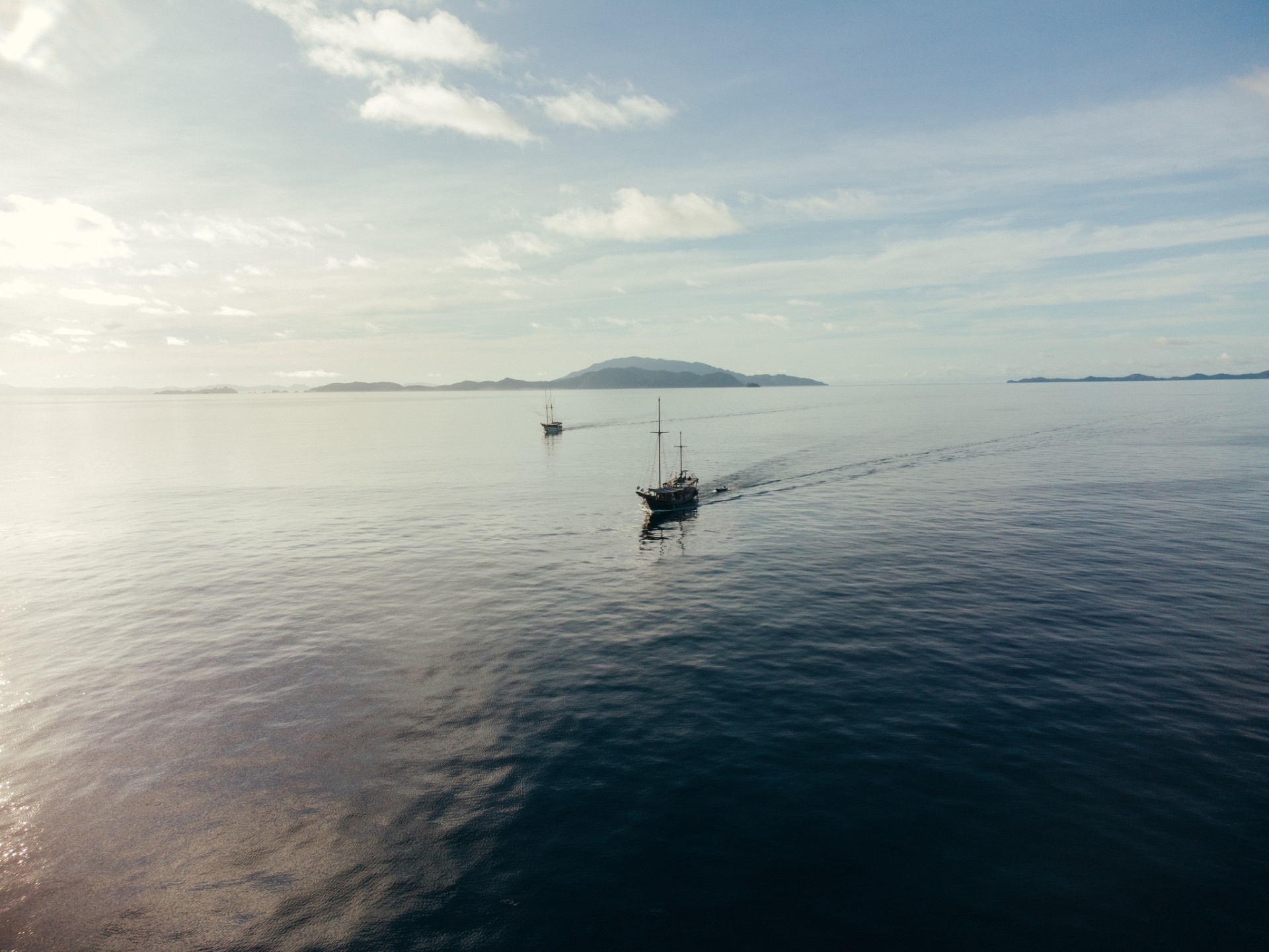 Senja cruising with a sister phinisi across calm open water toward distant islands