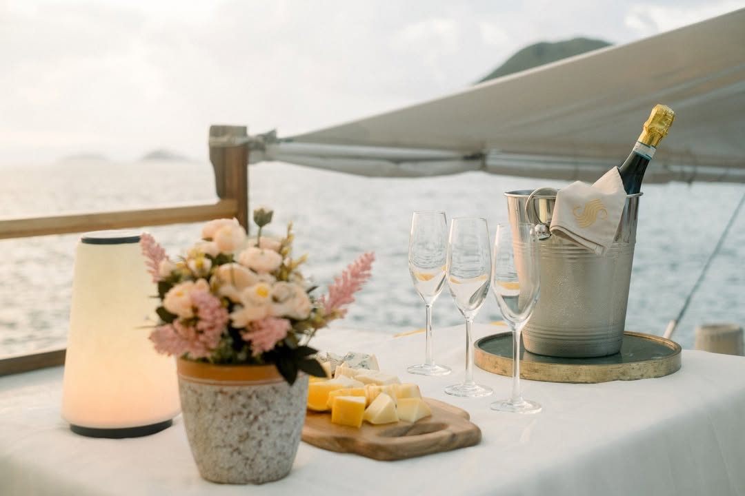 Champagne, glasses and cheese board set on Samara II's deck at golden hour with the sea beyond