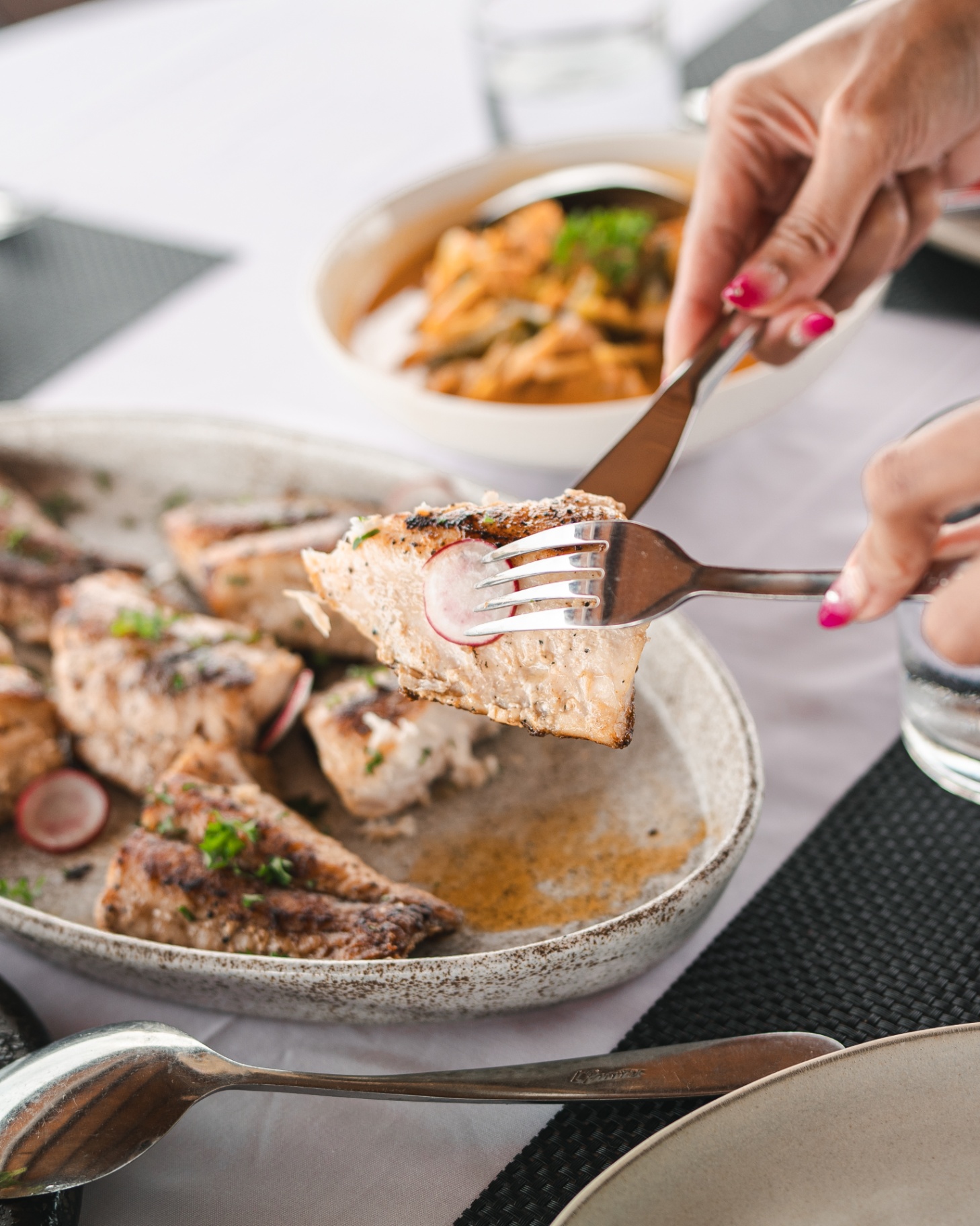 Guest lifting a forkful of grilled fish over a platter of seared fillets in Mischief's dining area