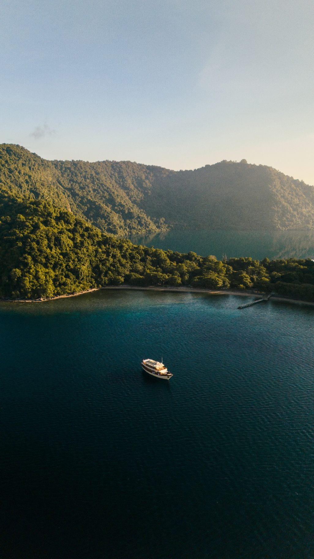 Mischief anchored in a jungle-lined cove at golden hour in Raja Ampat