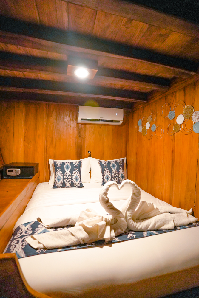 Cosy double cabin on Adishree with warm teak walls, ikat cushions and towel swans