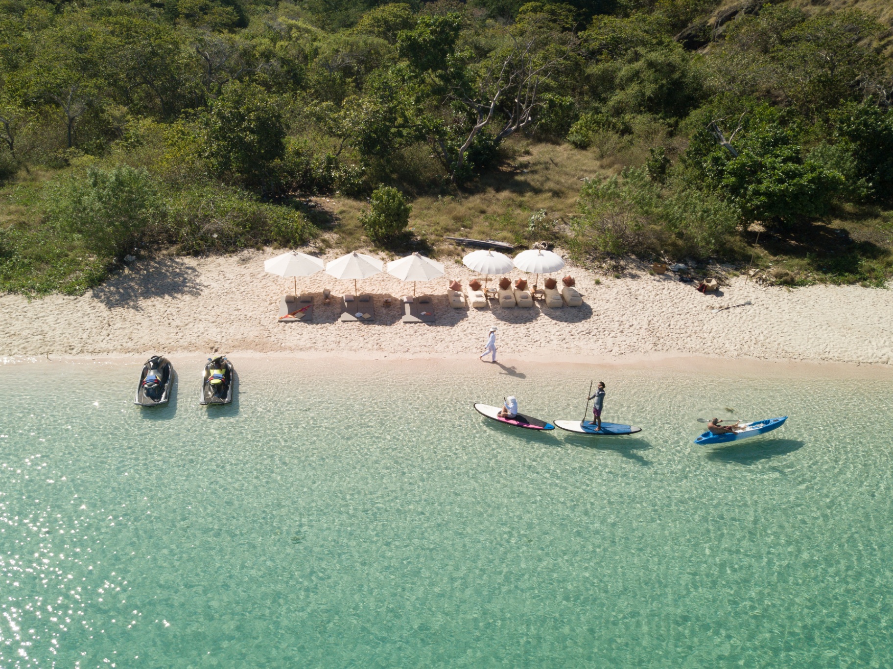 Aerial view of Lamima's beach club with jetskis, paddleboards and kayak lined up on clear turquoise shallows in front of parasols and loungers