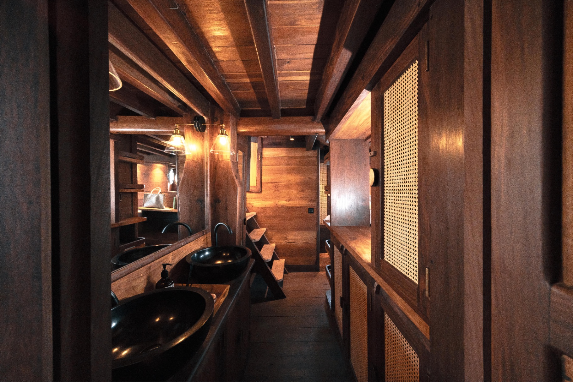 Master ensuite on Nataraja with twin black stone basins, warm wood panelling and cane cabinet doors