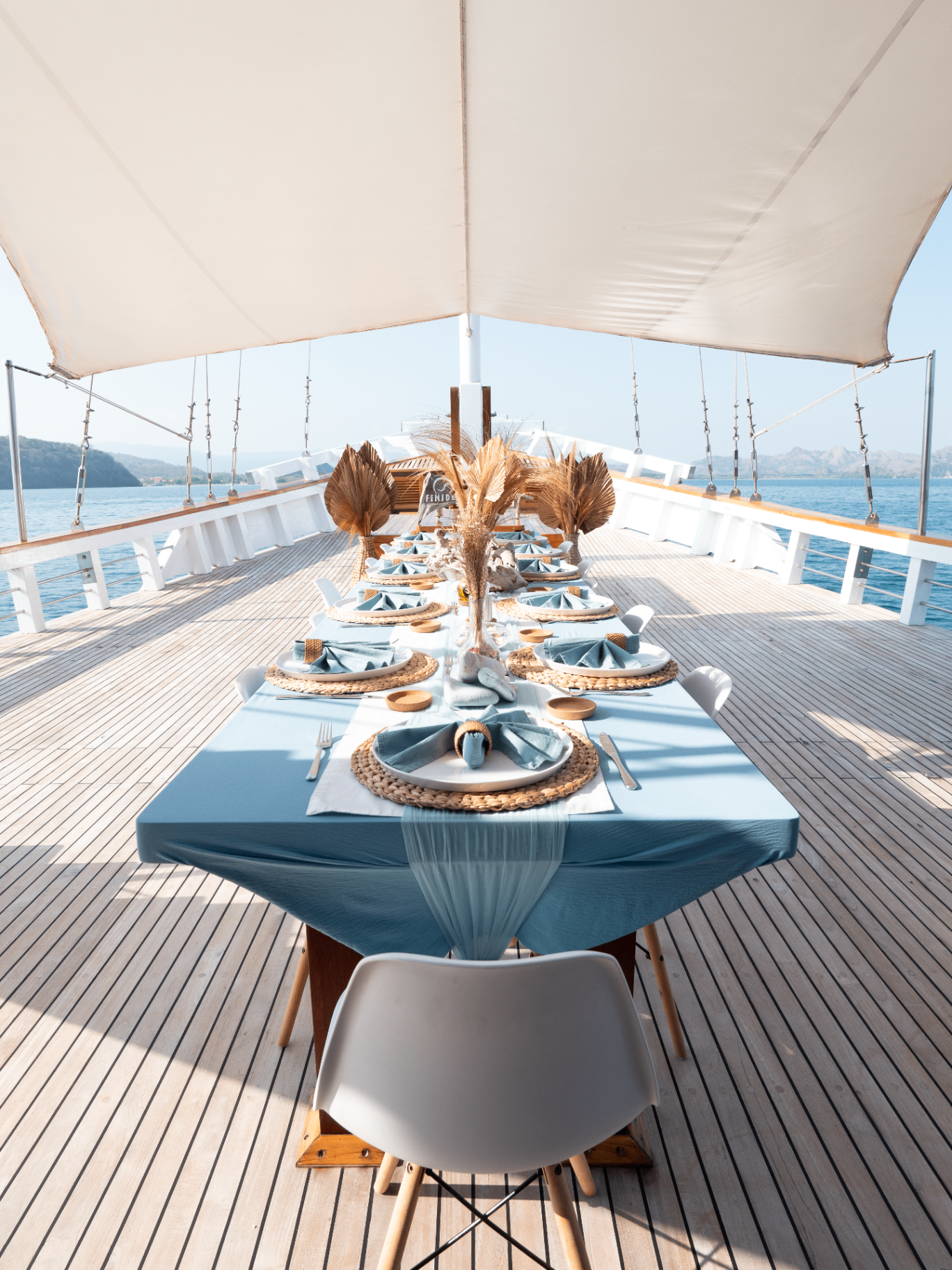 Long deck dining table set with blue linen under a canopy on Fenides