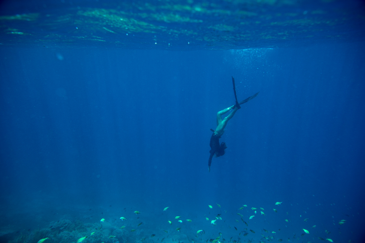 Freediver descending into clear blue water above a reef
