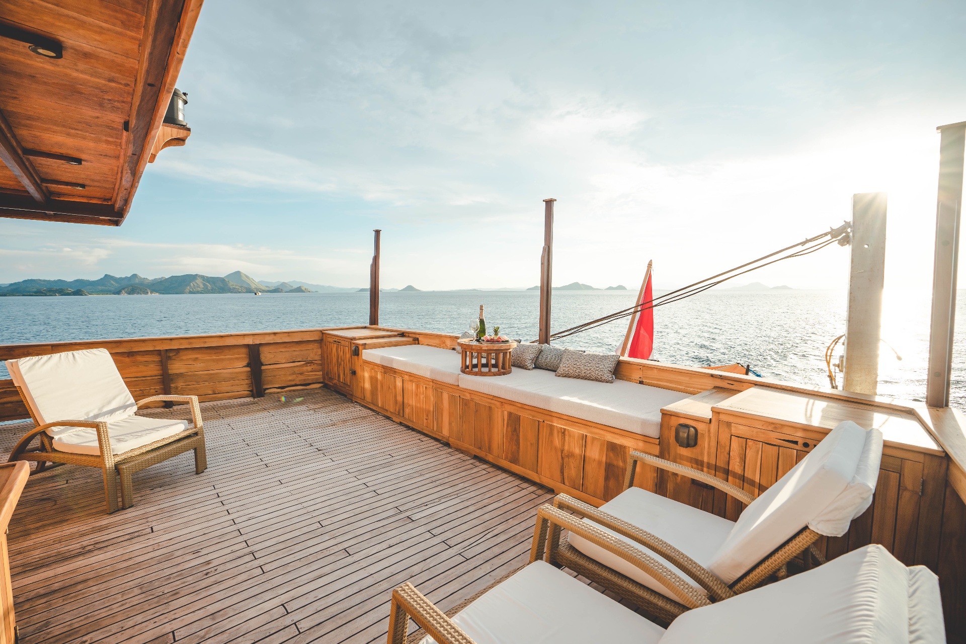 Mischief bow lounge at golden hour with daybed, sun loungers and champagne overlooking Komodo National Park