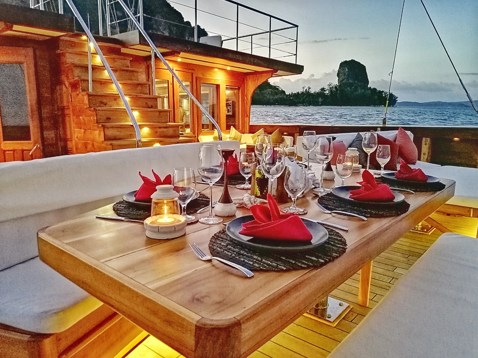 Candlelit alfresco dinner table set on Lamima's aft deck at sunset with limestone karst in the distance